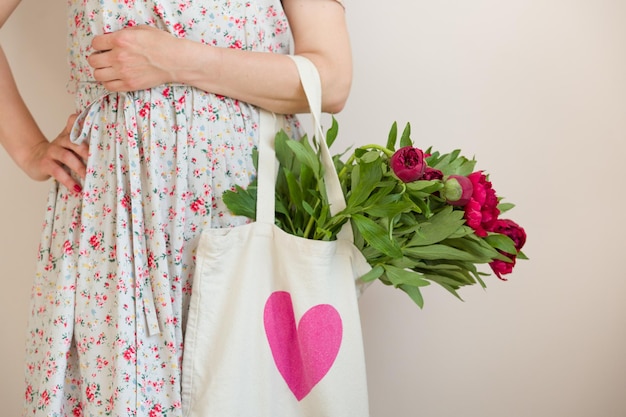 Donna che tiene una borsa in tessuto con un bel mazzo di peonie rosse