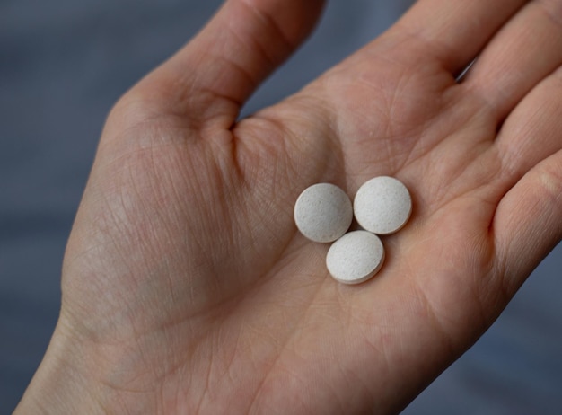 A woman holding three white round pills in her hand