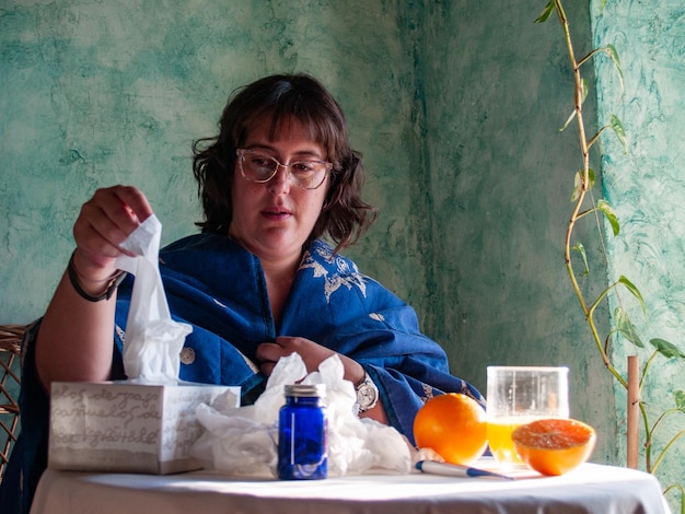 Woman holding tissue paper by oranges on table at home