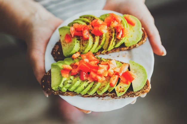 Woman holding toasts with avocado and tomatoes on plate.