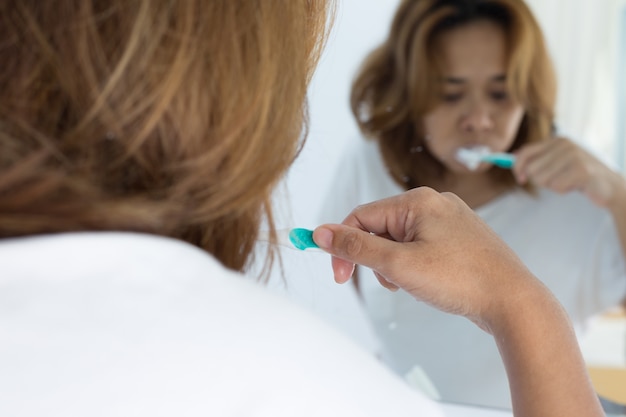 женщина, держащая зубную щетку и зубы кисти, отражается в зеркале
