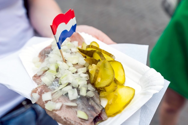 Woman holding traditional Dutch snack with raw herring with pickles.