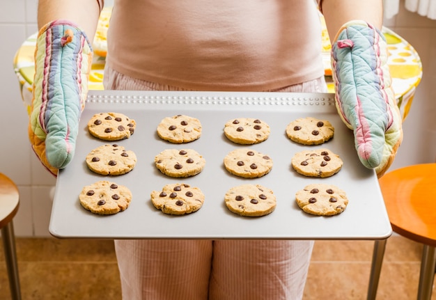 Photo woman holding a tray with homemade baked cookies with colorful kitchen gloves