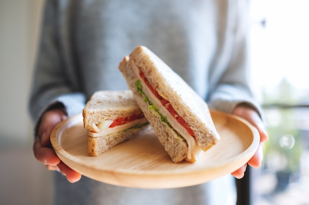 Photo a woman holding two pieces of whole wheat sandwich in wooden plate