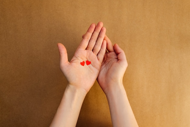 Woman holding two small paper hearts on palms.