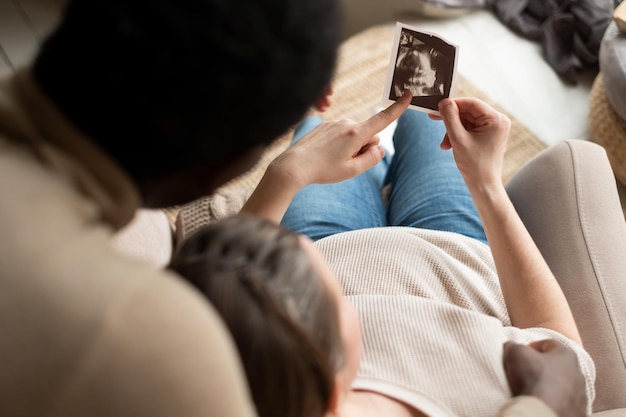 Woman holding ultrasound image of her baby showing her husband details on it Pregnancy and future parenthood concept