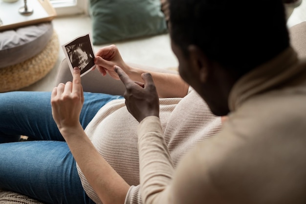 Woman holding ultrasound image of her baby showing her husband details on it Pregnancy and future parenthood concept