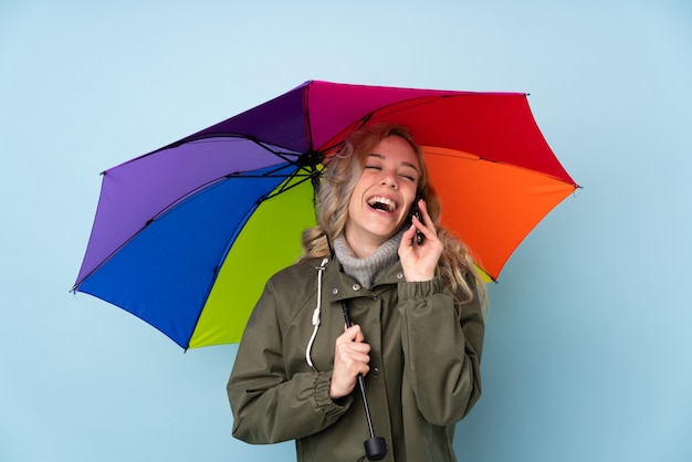 Woman holding an umbrella isolated on blue wall