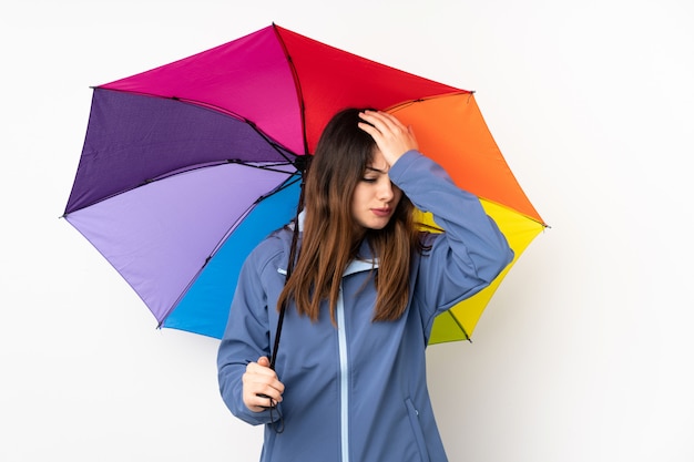 Woman holding an umbrella on white wall having doubts with confuse face expression