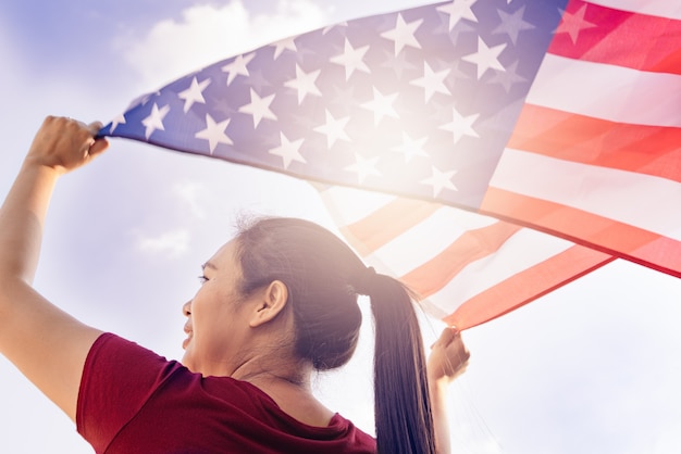 Woman holding United States of America flag on sunny sky. USA Memorial day and Independence day concept.