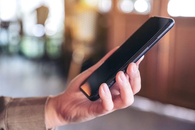 A woman holding and using a black smartphone in cafe