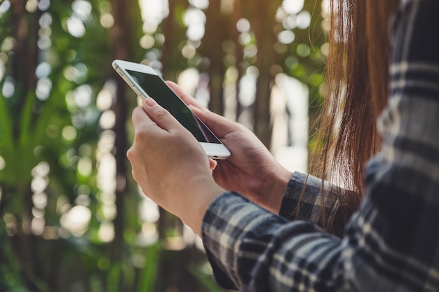 a woman holding, using and looking at smart phone with blur green nature background