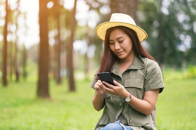 Женщина, держащая и использующая мобильный телефон, сидя в парке