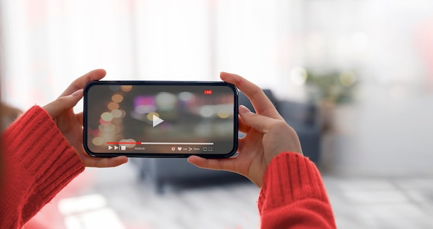 Woman holding and watching video via mobile phone in horizontal view at home