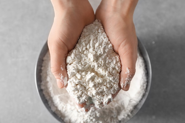 Woman holding wheat flour above bowl on table closeup