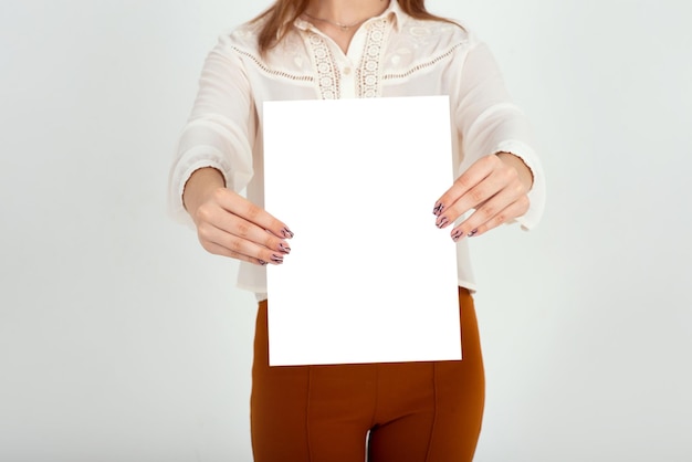 Photo woman holding a white blank sign in her hands on a light background