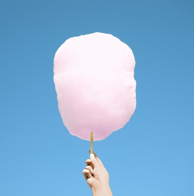 Woman holding white cotton candy against blue sky