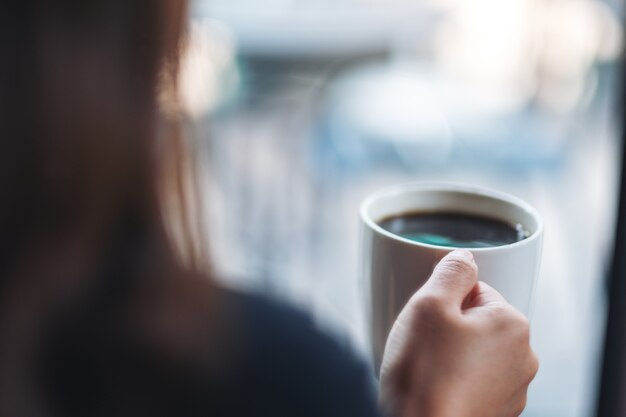 A woman holding a white cup of hot coffee with blurred background