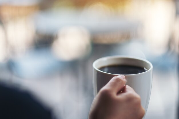 A woman holding a white cup of hot coffee with blurred background