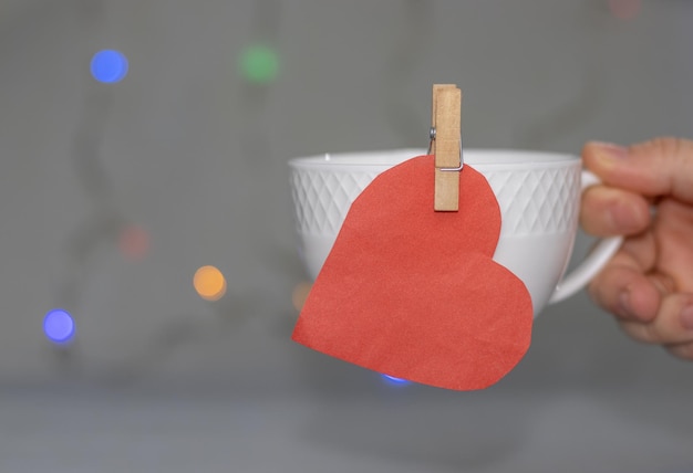 woman holding white cup with red paper heart attached with wooden clothespin valentines day