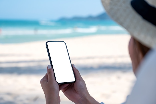 ビーチで青い空の背景と空白のデスクトップ画面で白い携帯電話を保持している女性