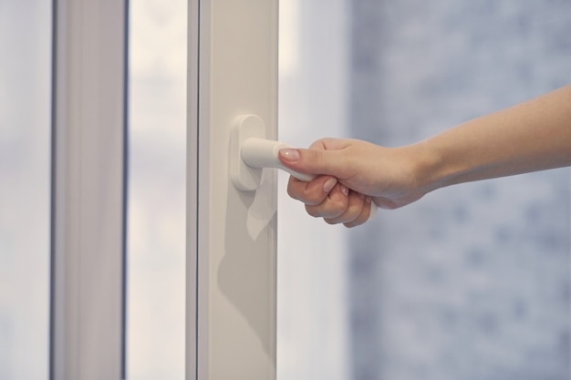 Woman holding white modern handle at PVC plastic window with double glazing, opening and closing frame