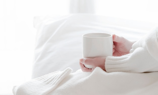 Woman holding a white mug while sitting on the bed