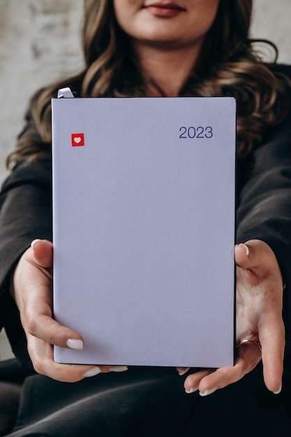 A woman holding a white notebook with the number 2023 on it.