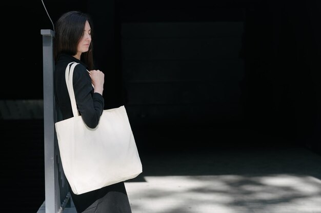 Woman holding white textile eco bag against urban city background Ecology or environment protection concept White eco bag for mock up