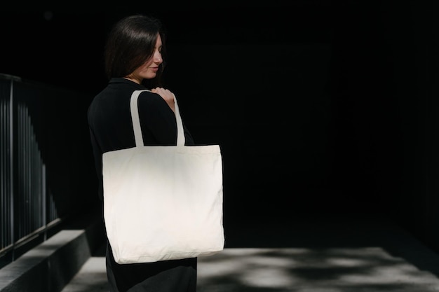 Woman holding white textile eco bag against urban city background Ecology or environment protection concept White eco bag for mock up