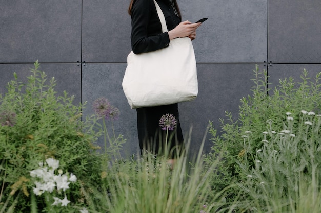 Woman holding white textile eco bag against urban city background Ecology or environment protection concept White eco bag for mock up