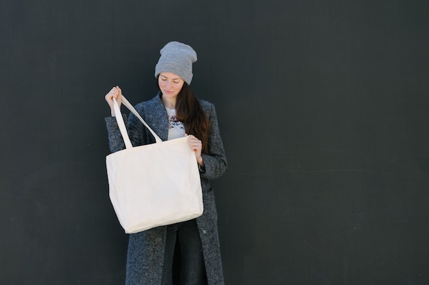 Woman holding white textile tote eco bag in urban area