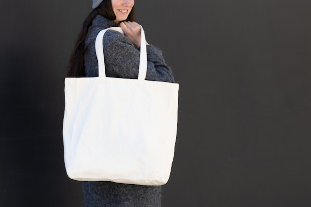 Woman holding white textile tote eco bag in urban area