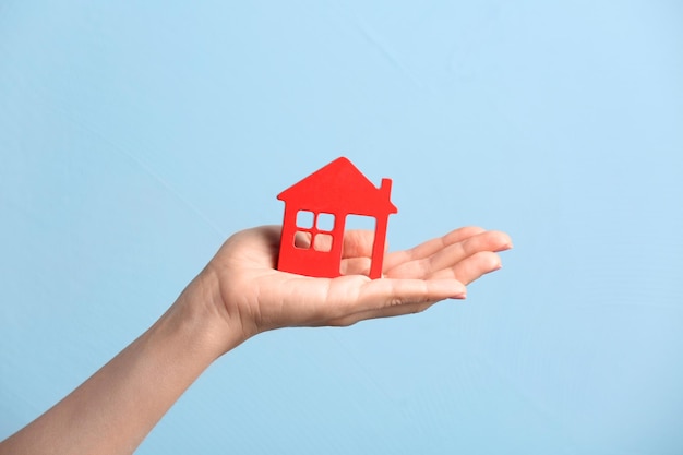 Woman holding wooden figure of house on color background