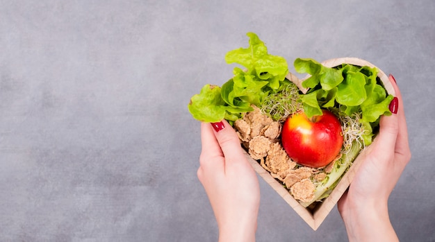 Photo woman holding wooden heart with apple and cereals