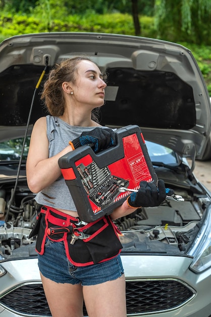 Woman holding work tools standing near broken car and waiting\
for help female driver is confused and doesnt know what to do