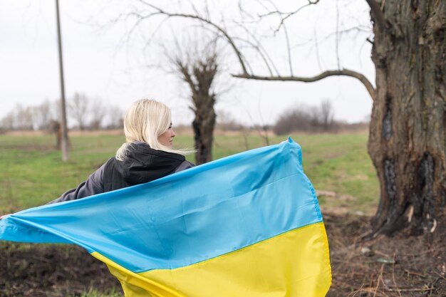 焼けた木の背景にウクライナの黄色と青の旗を保持している女性