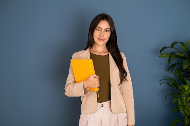 A woman holding a yellow folder in front of a blue wall