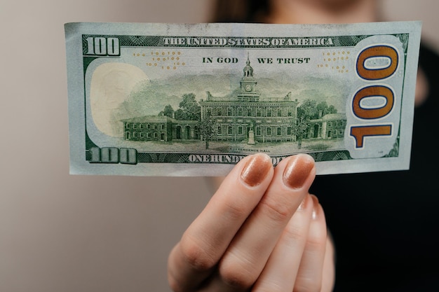 A woman holds 100 dollar bills in front of her