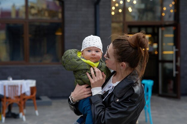 A woman holds a baby in a green jacket and a black jacket.