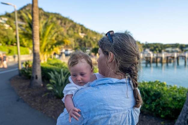 A woman holds a baby in her arms, the palm tree is in the background.