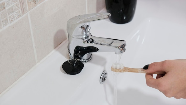 Woman holds a bamboo toothbrush under the tap with running water. Seen from above