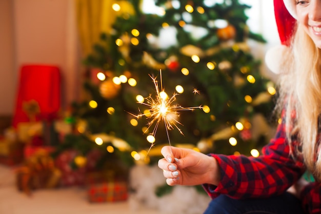 Woman holds the bengal light over defocused Christmas tree, holiday evening