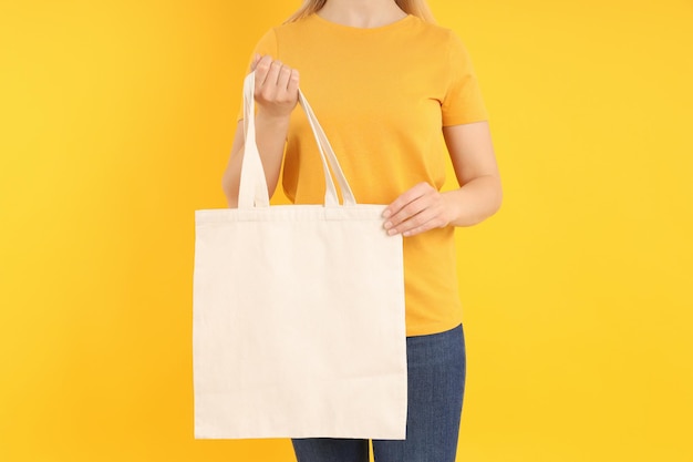 Woman holds blank cotton bag on yellow background