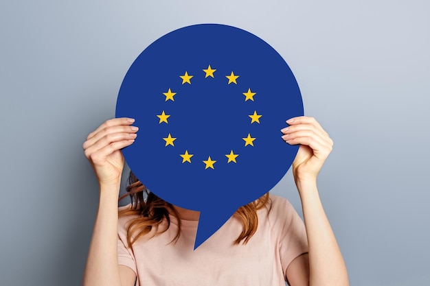 Photo woman holds blank white speech bubble with european union flag isolated over grey studio background news information channel concept