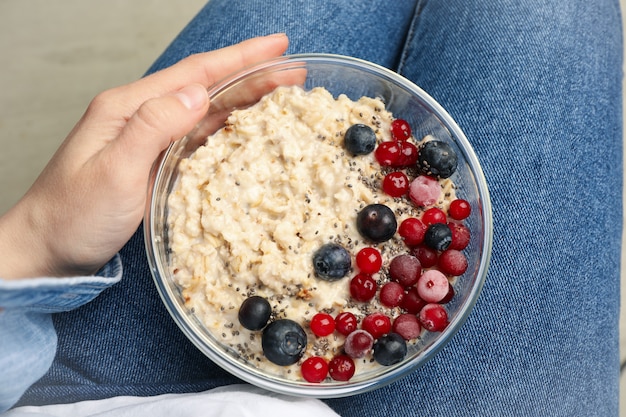 Woman holds bowl with oatmeal porridge with fruits, top view