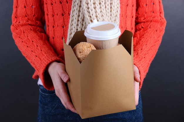 女性は黒い背景にコーヒーとクッキーの入った箱を持っている