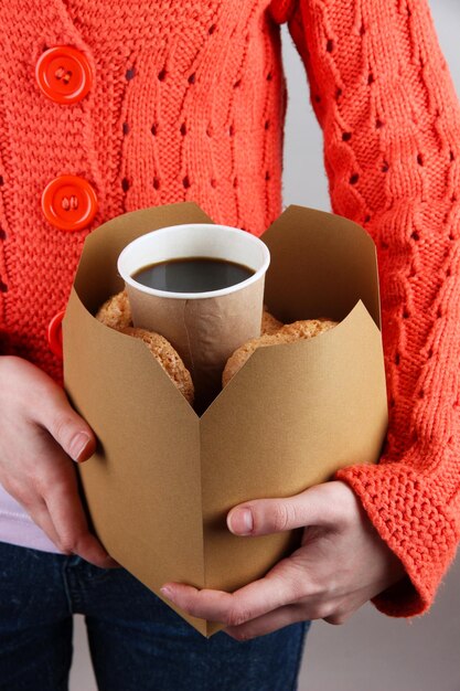 Woman holds box with coffee and cookies on grey background