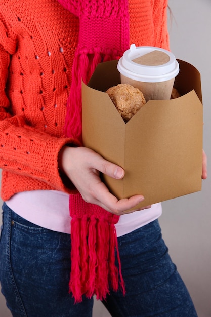 Foto la donna tiene la scatola con caffè e biscotti su sfondo grigio