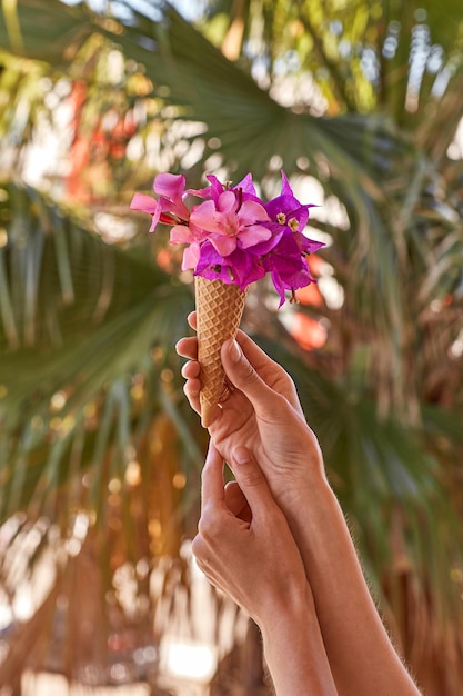 Woman holds bright pink flowersBougainvillea in an ice cream cone in the background of palm leaves